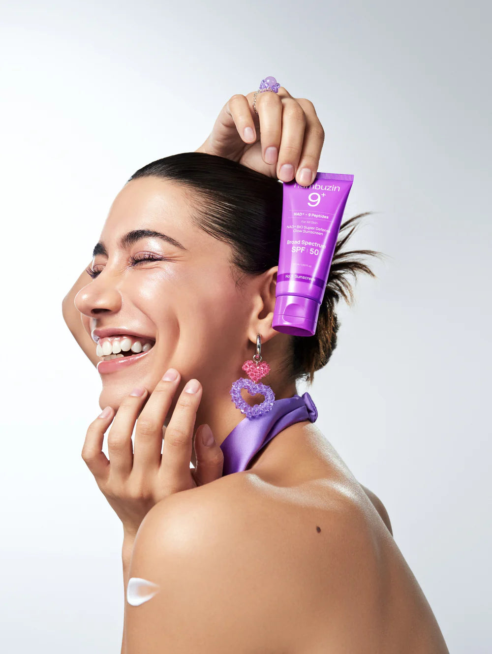 Woman applying sunscreen with a purple bottle on a white background